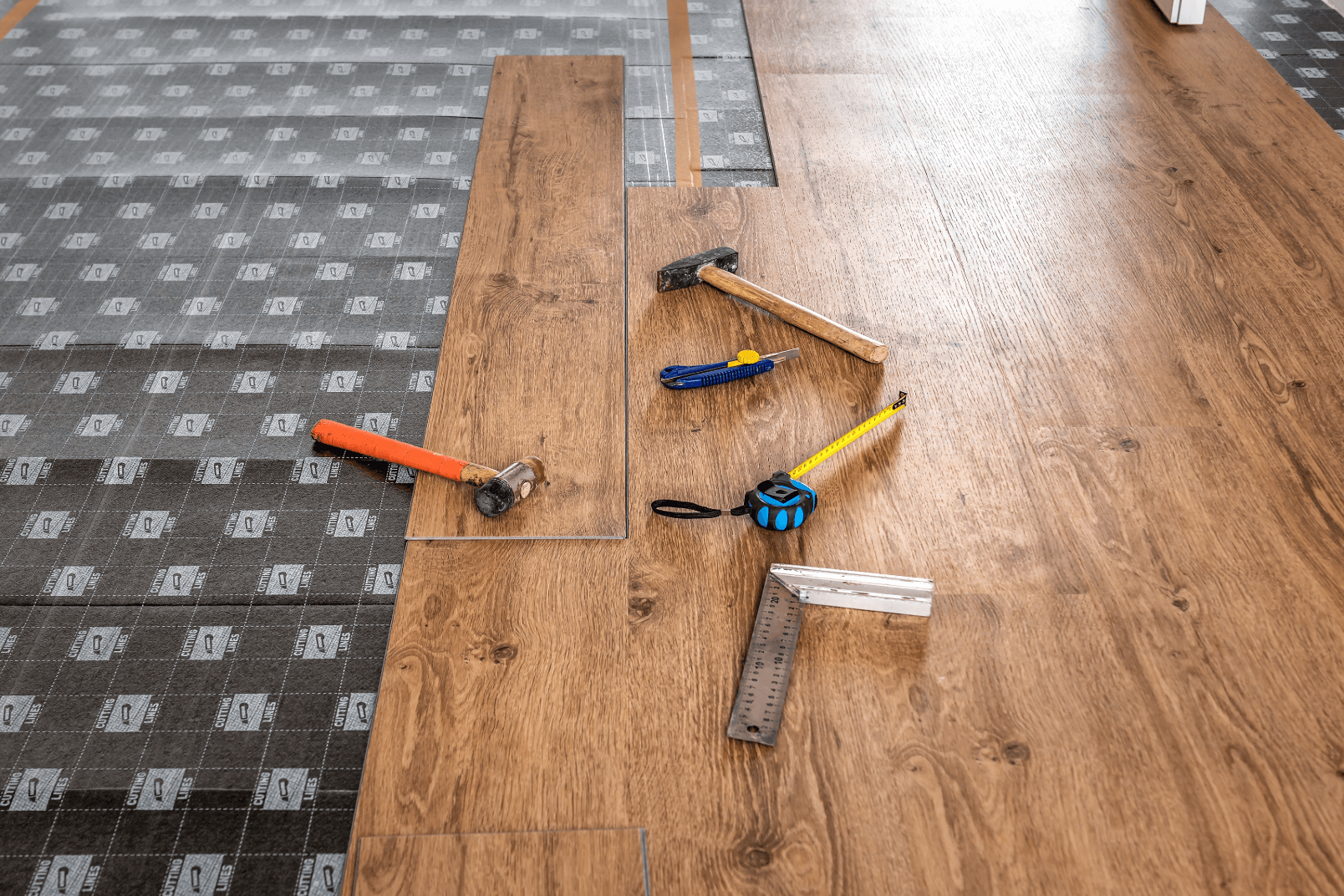 Vinyl wood plank flooring being installed with tools resting on top.
